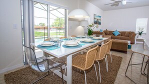 A dining area with a table set for four, clear glass chairs, and a large window with curtains.
