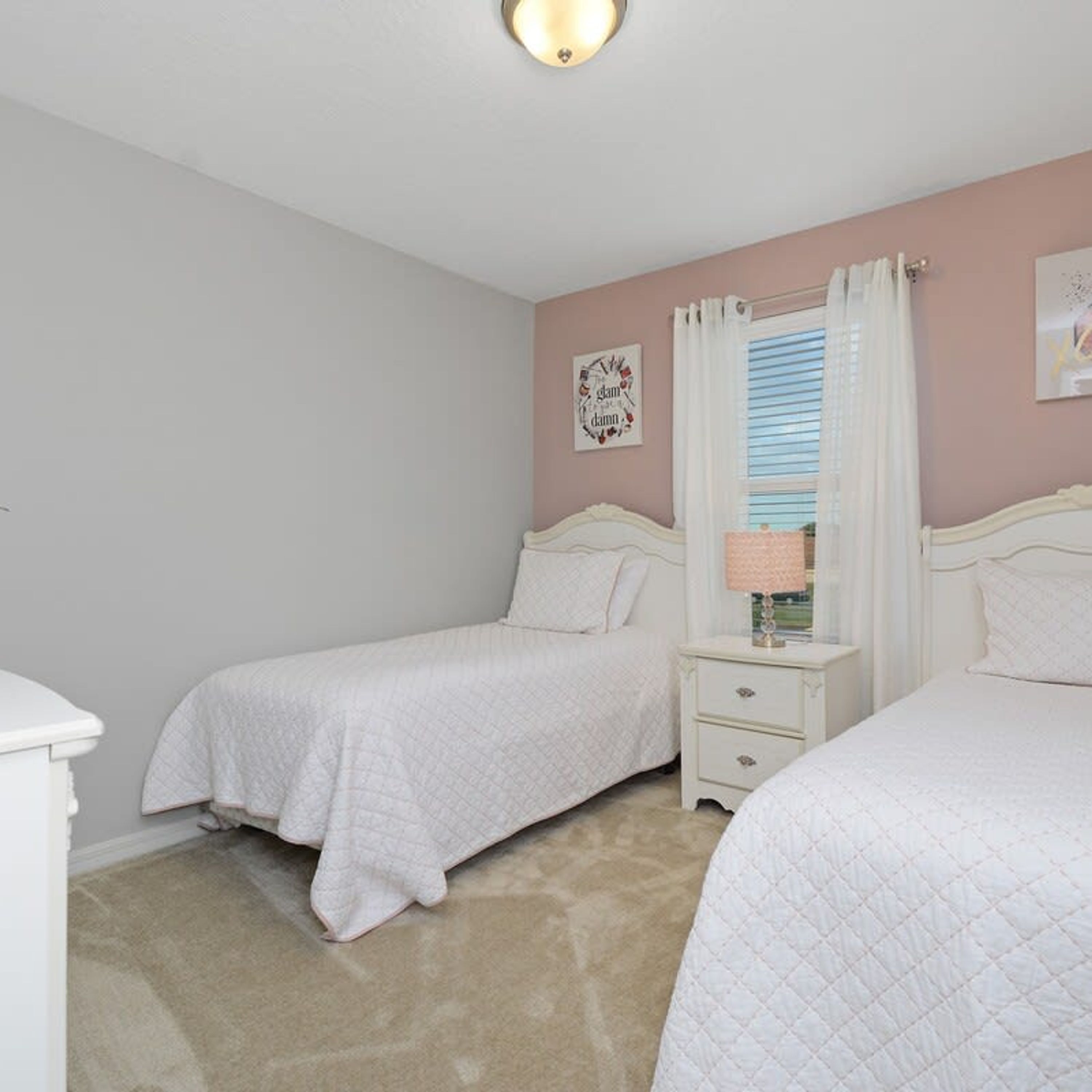A bedroom with two beds, a nightstand, a window with curtains, and a wall decoration.