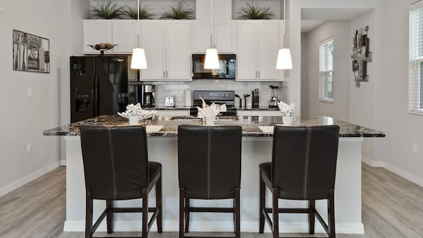 A modern kitchen with white cabinets, a central island with bar stools, and pendant lighting. - Four Bedroom Gameroom Compass Bay Resort 5128a (Kissimmee)