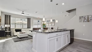A modern kitchen with white cabinetry, a large island, pendant lighting, and a view to the outside. - Four Bedroom Gameroom Compass Bay Resort 5128a (Kissimmee)
