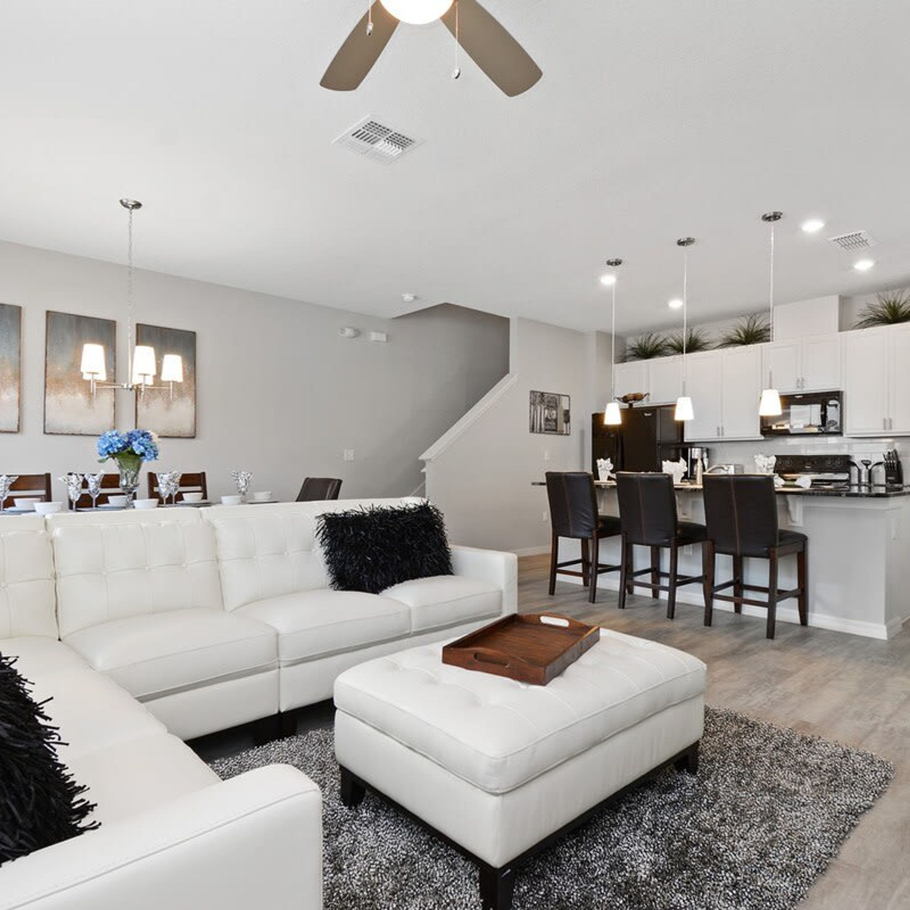 A modern living room with a white sofa, a coffee table, and a dining area with chairs and a kitchen in the background.