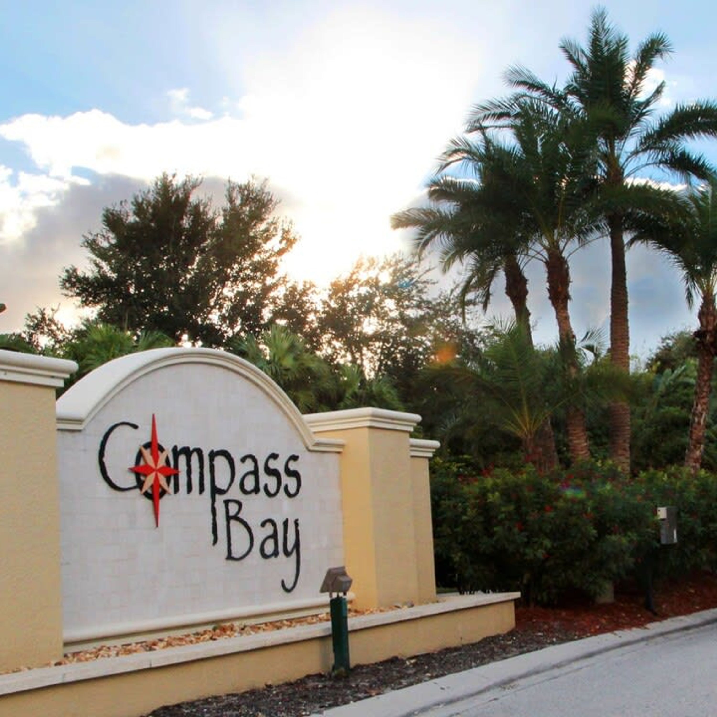 A sign with the text "Compass Bay" and a compass symbol, surrounded by palm trees and a clear sky.