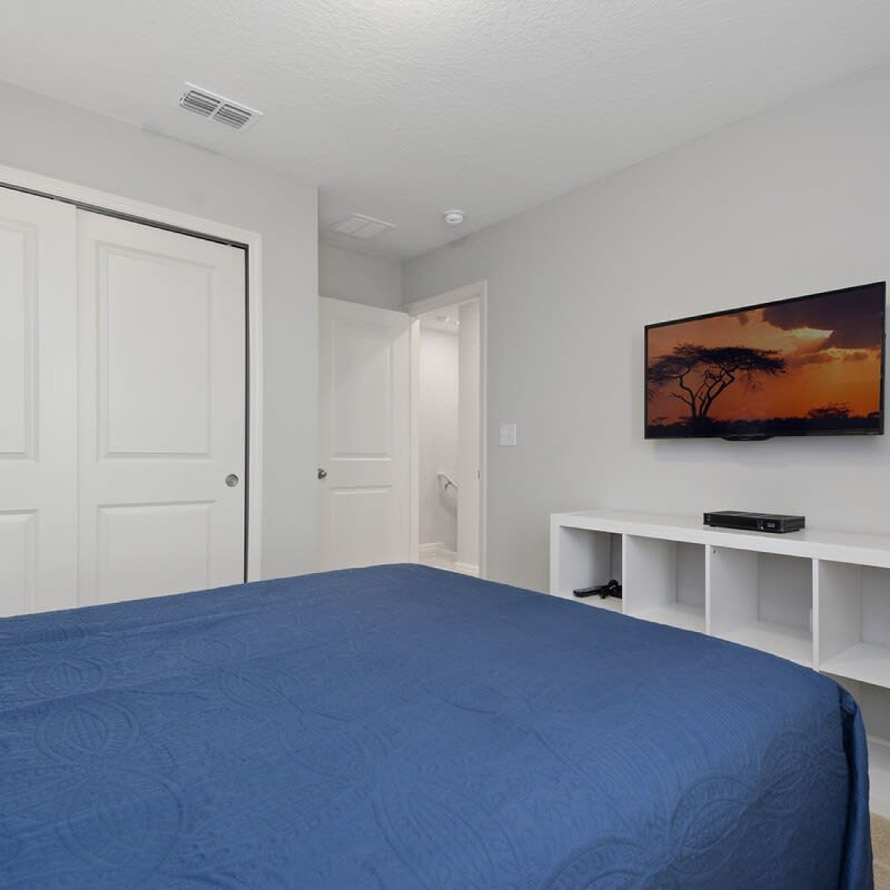 A bedroom with a large bed, a TV mounted on the wall, and a door leading to another room.