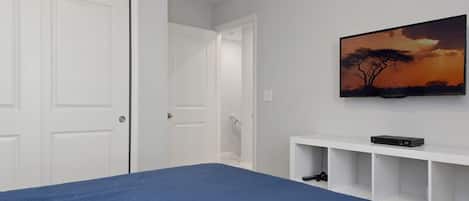A bedroom with a large bed, a TV mounted on the wall, and a door leading to another room.