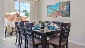 Comedor con una mesa dispuesta para cuatro personas, sillas, una araña y un cuadro en la pared.