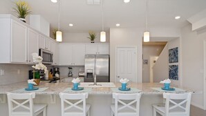 Una cocina moderna con armarios blancos, electrodomésticos de acero inoxidable y una isla central con taburetes de bar.