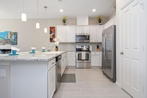 A modern kitchen with white cabinets, stainless steel appliances, pendant lighting, and a central island. - Four Bedroom Sleeps 10 w Gameroom 5152a (Kissimmee)