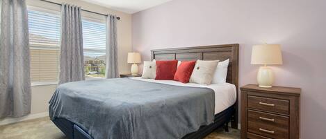 A bedroom with a bed, two bedside tables, a window with curtains, and a view outside.