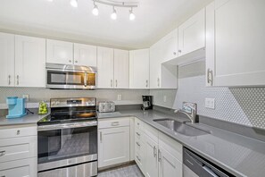 A modern kitchen with white cabinetry, a stainless steel oven, a microwave, a coffee maker, and a dishwasher.