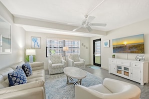 A living room with a sofa, two armchairs, a coffee table, a TV, and a ceiling fan.