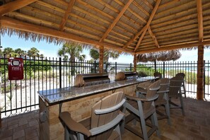 An outdoor barbecue area with a grill, seating, and a fire extinguisher. - A beachy dream: Steps from Siesta Key Beach. Gulf/ocean view from lanai. (Sarasota)