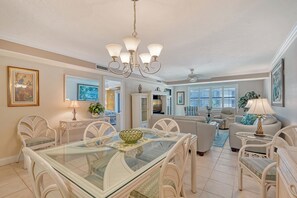 A spacious living room with a glass dining table, white wicker furniture, and a chandelier. - A beachy dream: Steps from Siesta Key Beach. Gulf/ocean view from lanai. (Sarasota)
