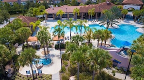 A resort with a large central pool, palm trees, and a building with a red-tiled roof. - Gorgeous 5 Bd w Pool Jacuzzi Close to Disney 6071 (Davenport)
