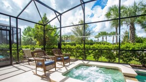 Een overdekte buitenzitplaats met een hottub, rieten stoelen en uitzicht op palmbomen en groen.
