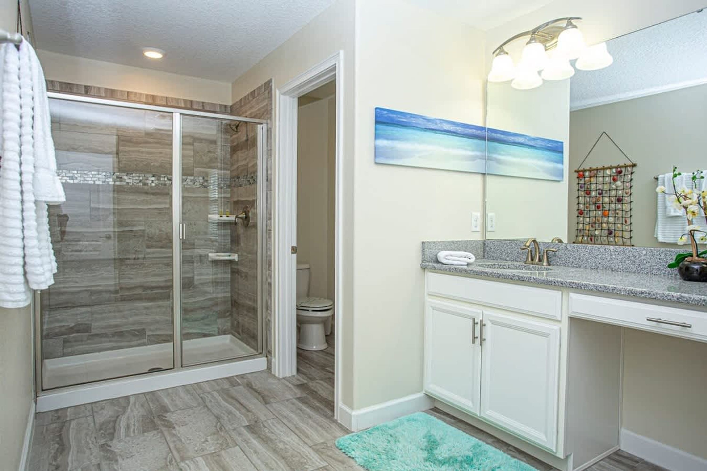 Une salle de bain dotée d’une douche à parois de verre, d’un lavabo avec un plan de travail en granit et d’un grand miroir.