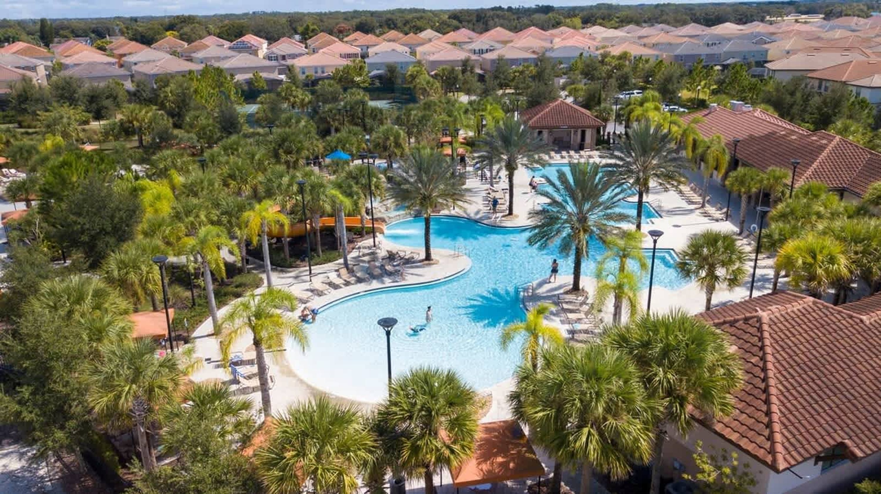 Un resort con una piscina grande, palmeras y vistas del barrio circundante.