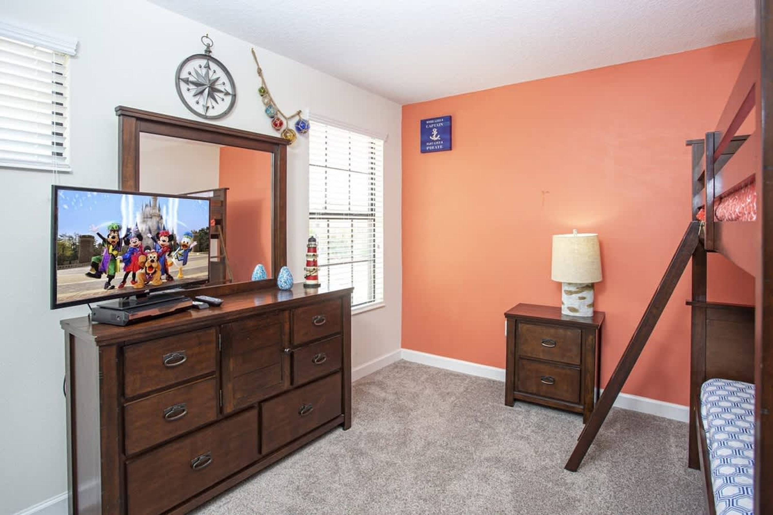 Een slaapkamer met televisie, dressoir, spiegel en stapelbed.