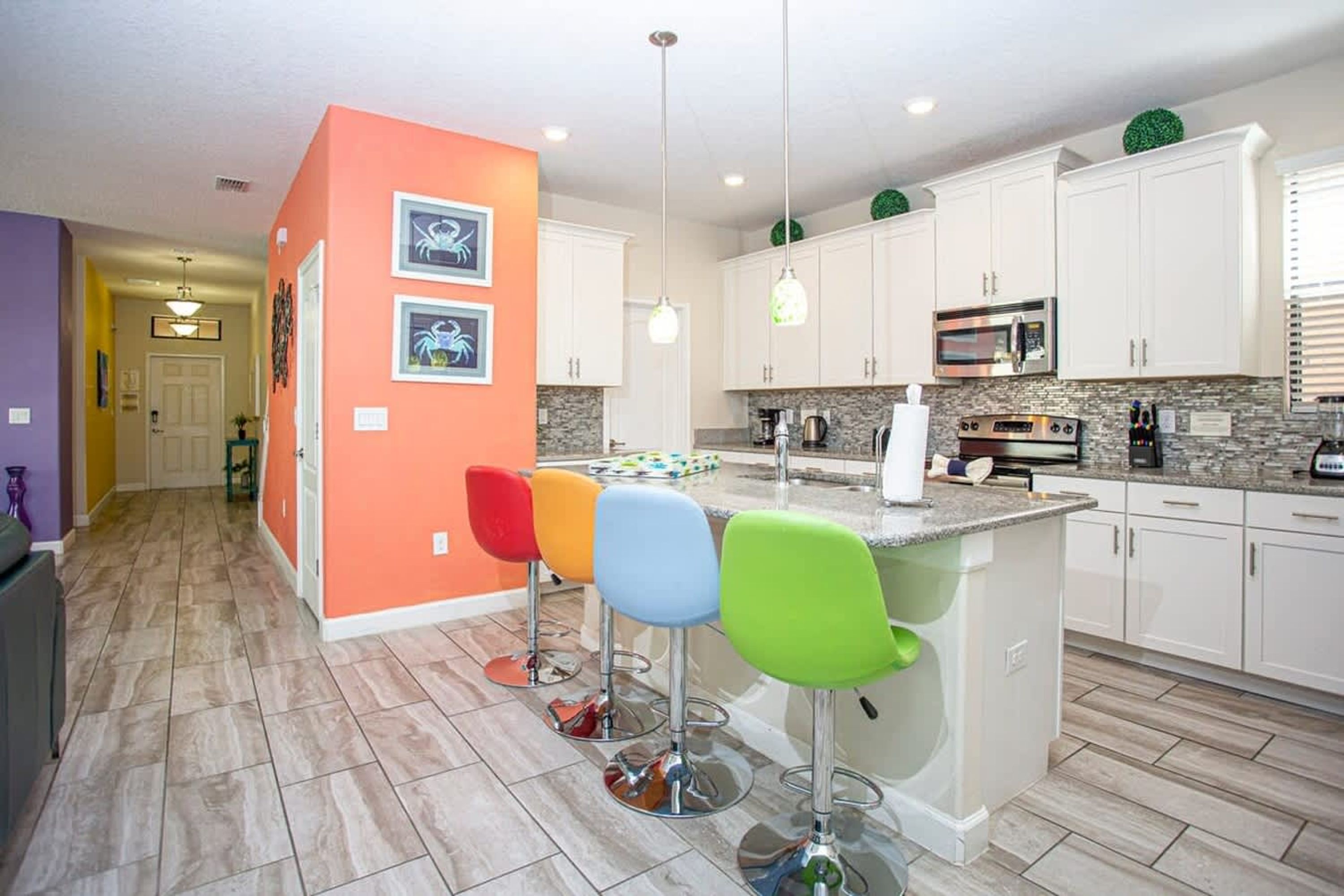 A modern kitchen with white cabinets, a central island with bar stools, and a microwave.
