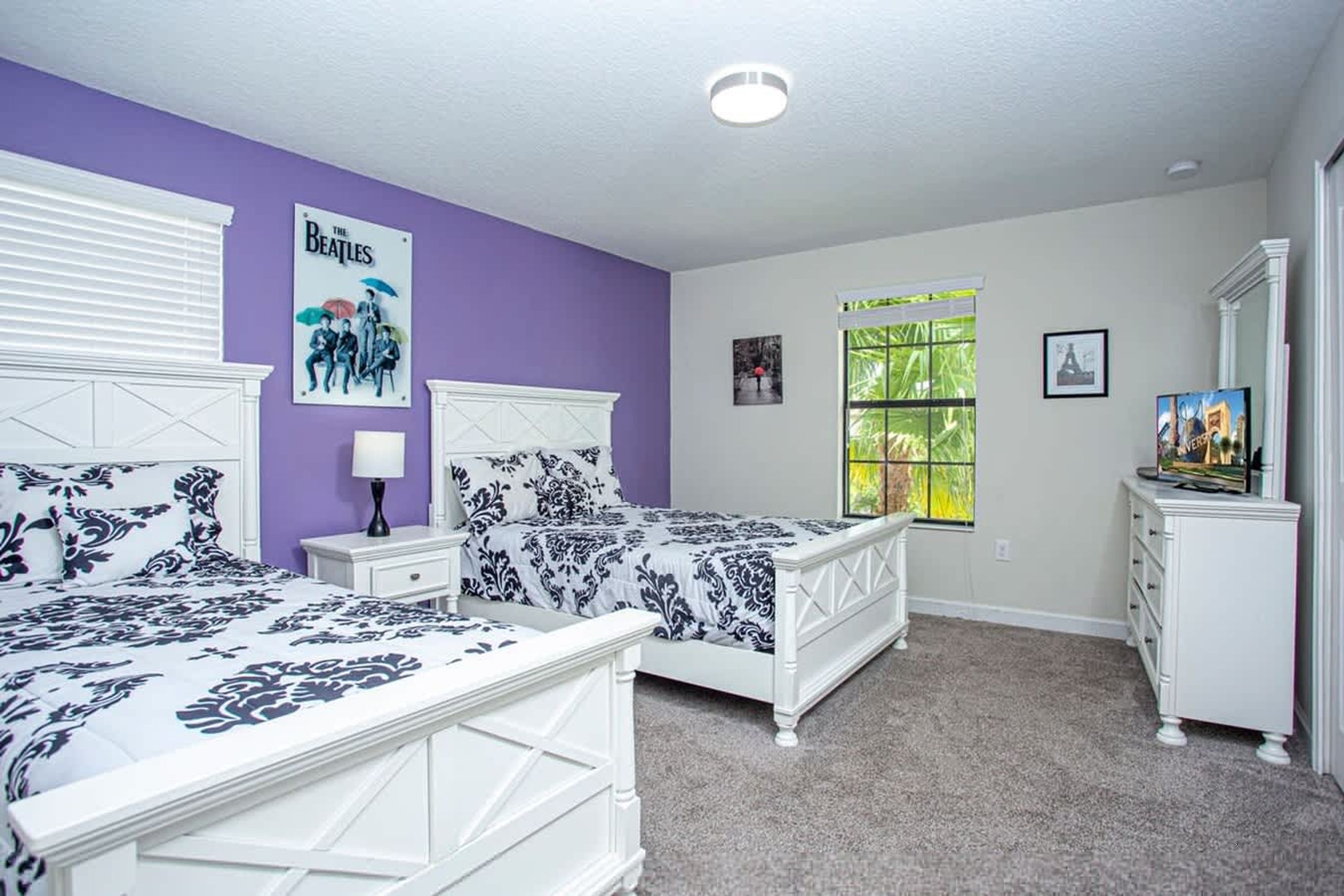 A bedroom with two beds, a dresser, a window with a view, and a poster on the wall.