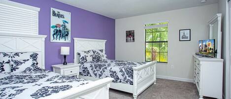 A bedroom with two beds, a dresser, a window with a view, and a poster on the wall.