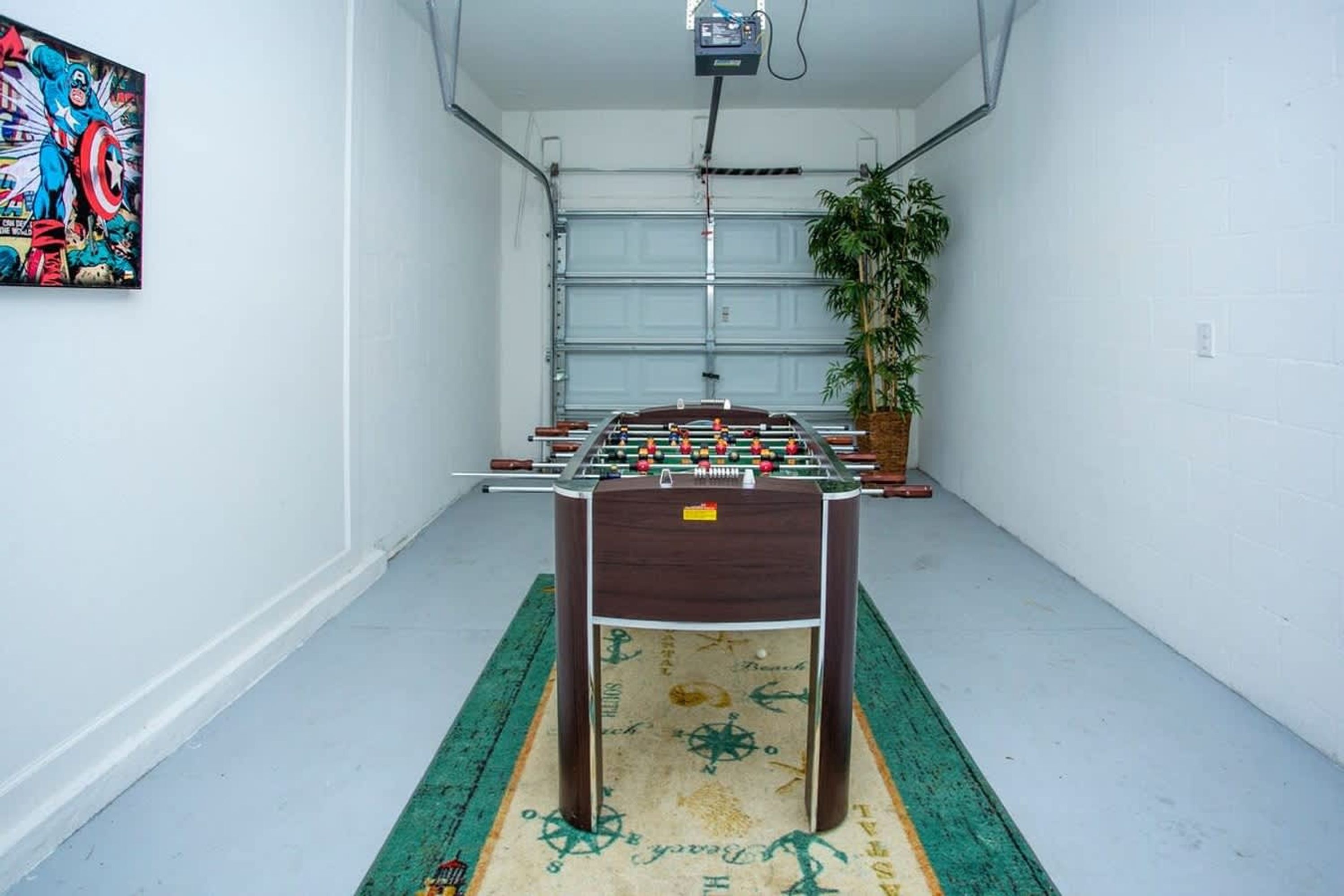 Ein Zimmer mit einem Fußballtisch, einer großen Pflanze und einem farbenfrohen Gemälde an der Wand.