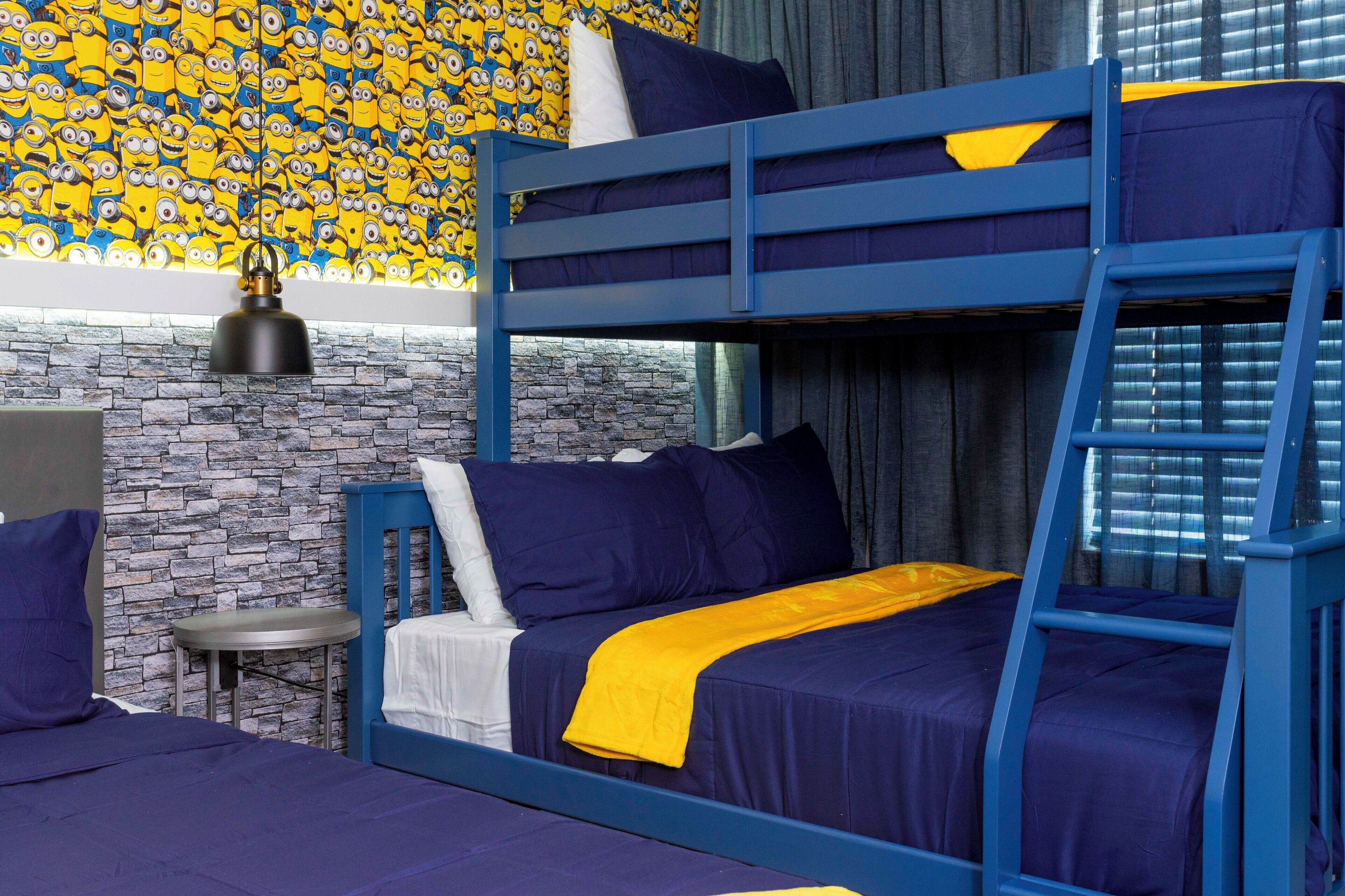 A bunk bed room with a stone wall, a small round table, and a Minion-themed wallpaper.