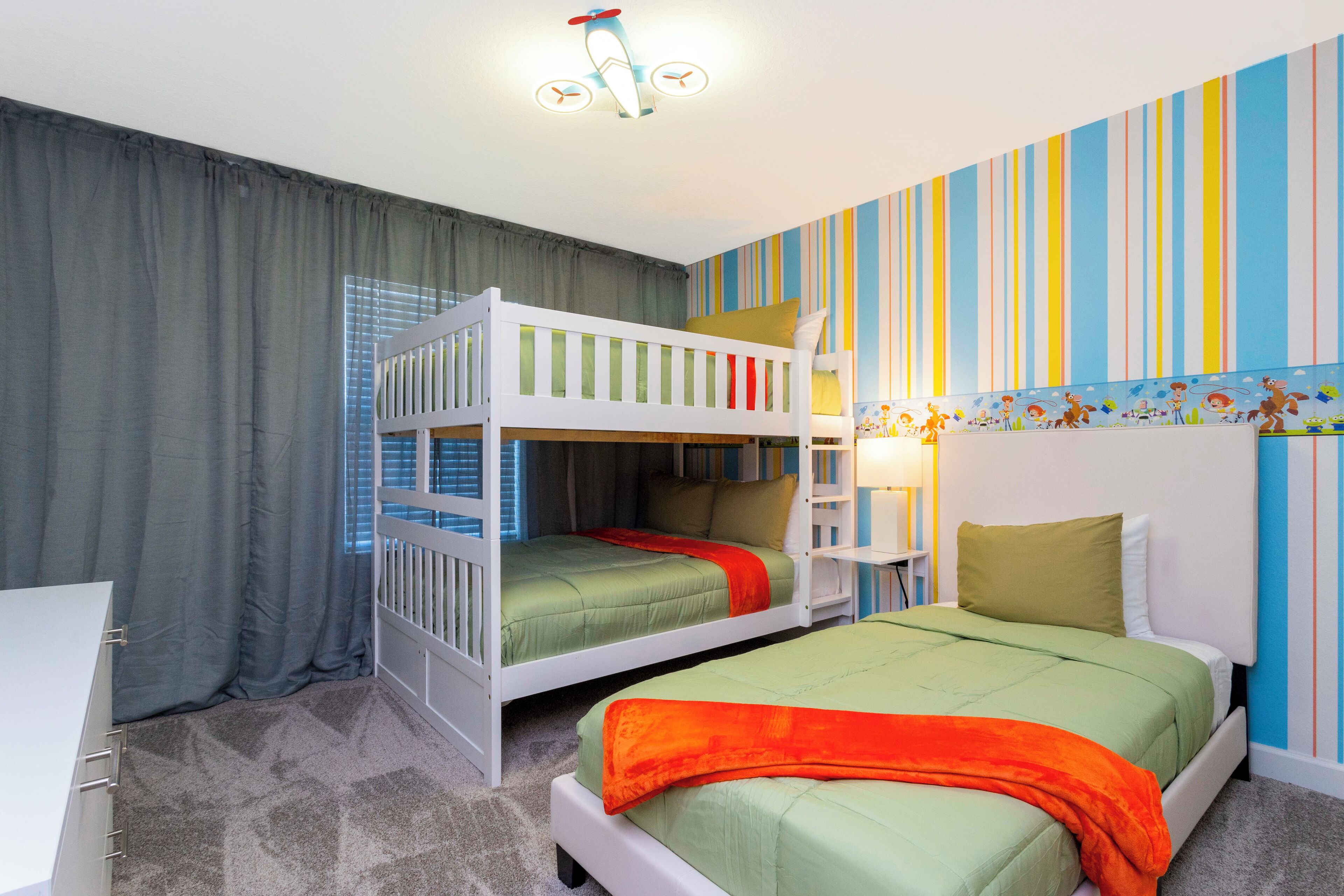 A bedroom with bunk beds, striped wallpaper, and a ceiling light fixture.