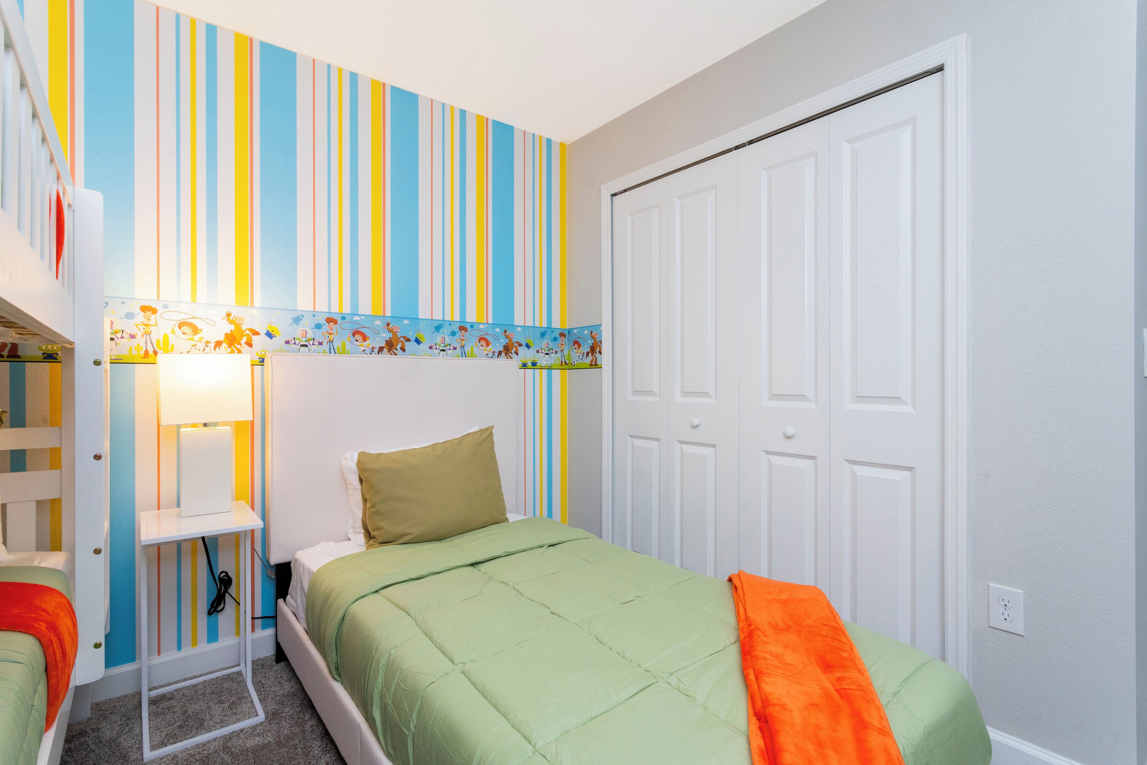 Quarto com uma cama beliche, uma cama de solteiro, papel de parede listrado e uma porta.