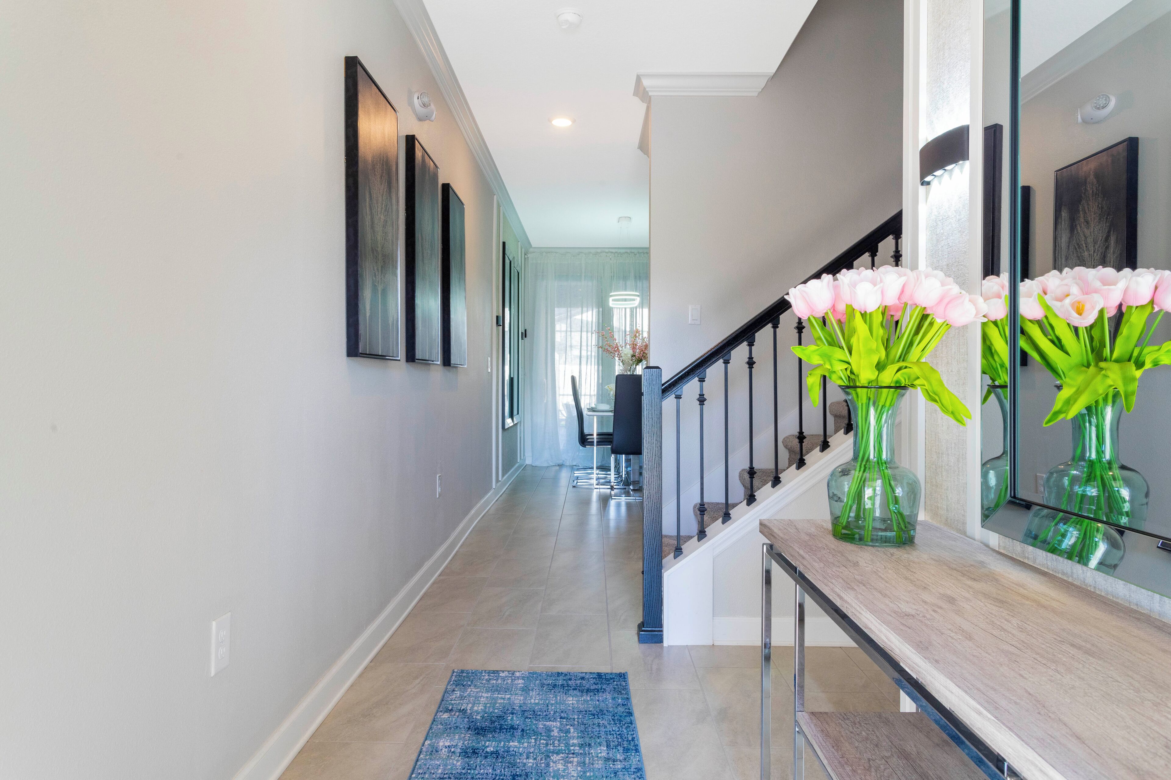 A modern hallway with a wooden bench, a blue rug, and a vase with pink flowers.