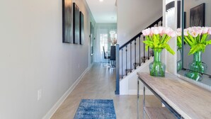 Un couloir moderne avec un banc en bois, un tapis bleu et un vase de fleurs roses.