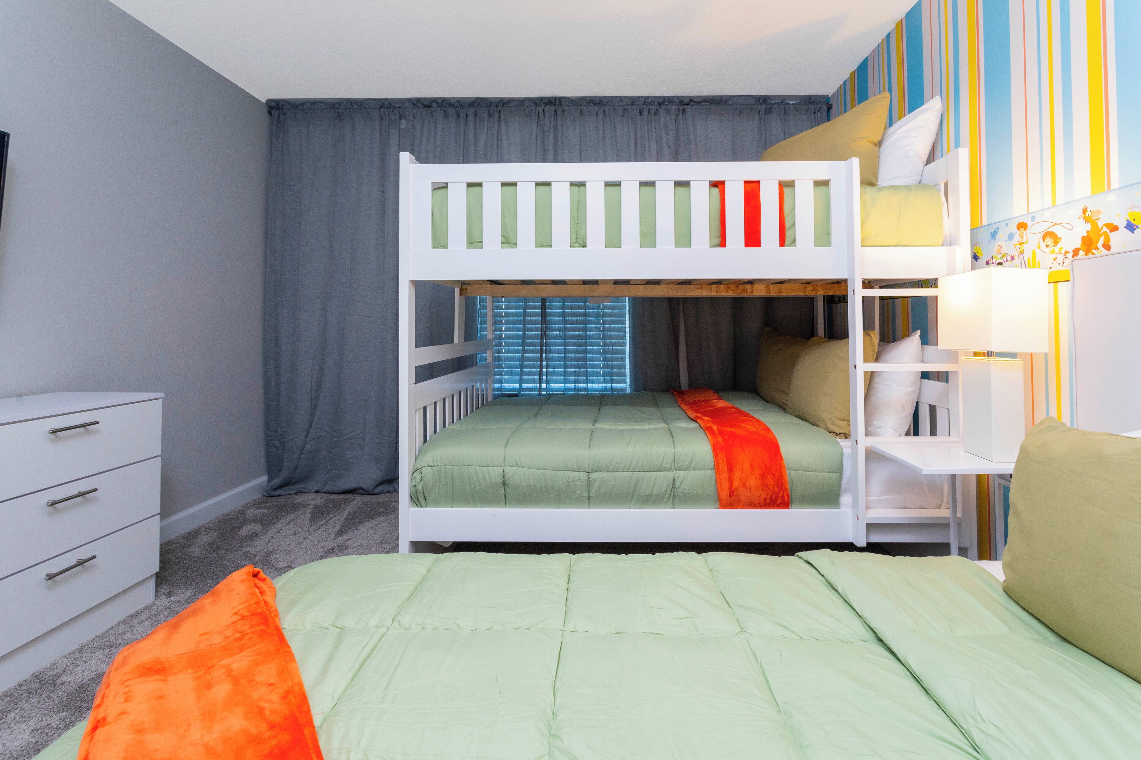 Une chambre avec un lit superposé, une fenêtre, une commode blanche et une bibliothèque.