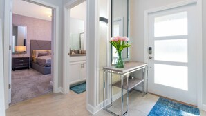 Une chambre moderne avec un lit, une table de chevet et un miroir. Un couloir mène à une autre pièce.