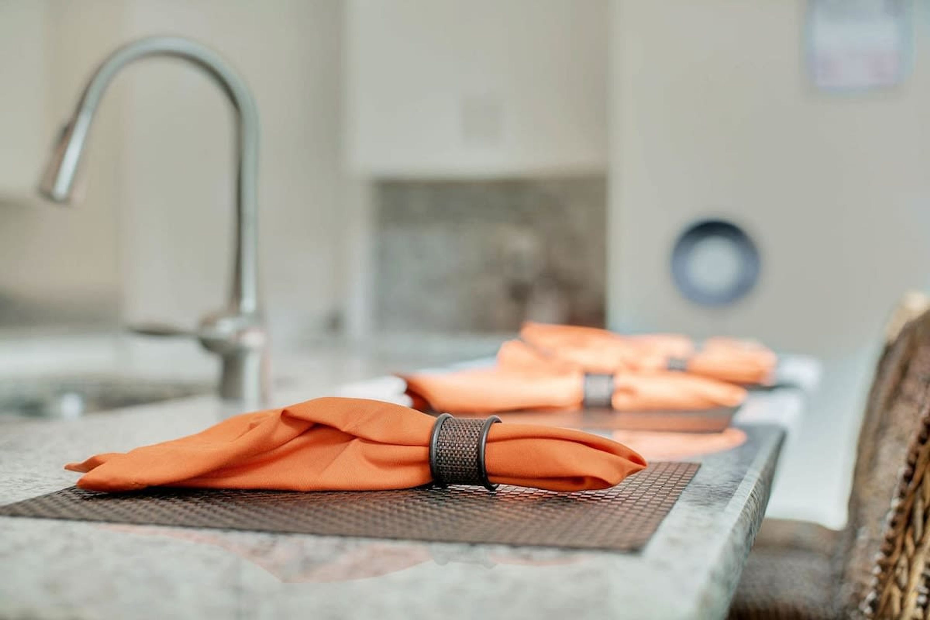 Una mesa ordenada con servilletas anaranjadas dobladas y un sujetador metálico para servilleta.