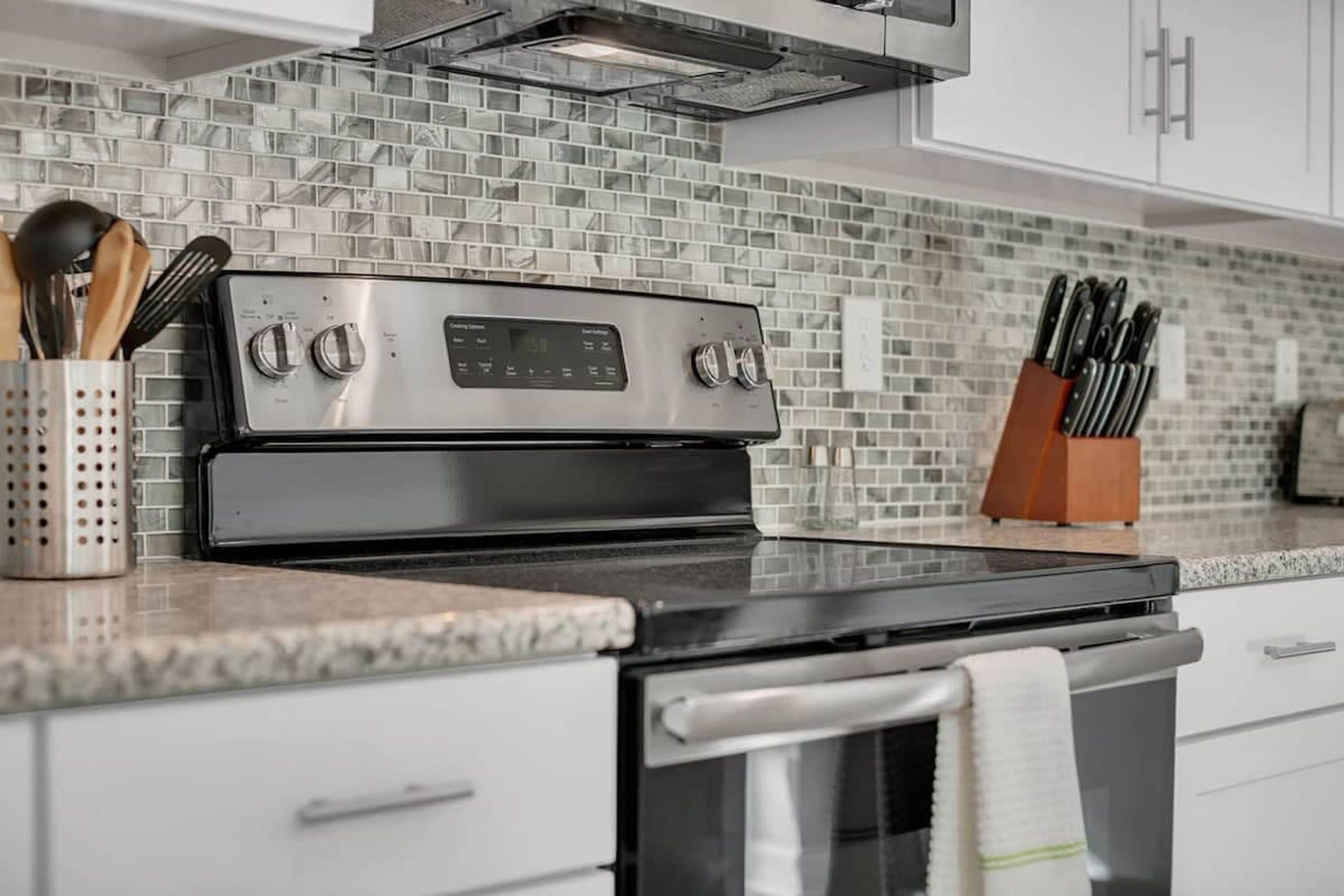 A kitchen with a stainless steel stove, a tiled backsplash, and a knife block on the countertop.