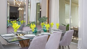 Uma sala de jantar moderna com mesa de vidro, cadeiras estofadas cinzentas e guardanapos amarelos.