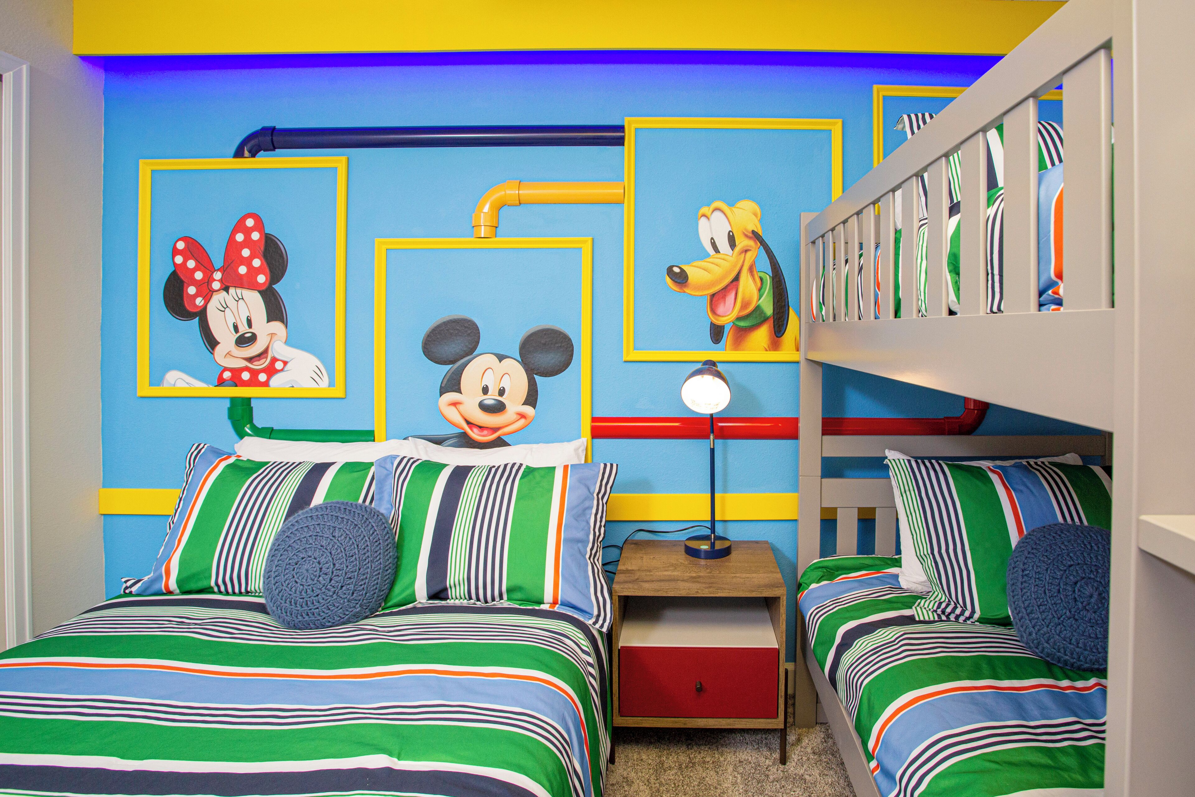 A children's bedroom with two beds, colorful striped bedding, Mickey Mouse and Minnie Mouse wall art, and a bunk bed on the right.