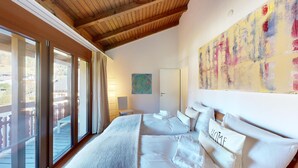 A bedroom with a large bed, a view through the window, and a painting on the wall.