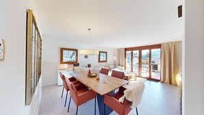 A spacious dining area with a long table, multiple chairs, and a view of the outdoors through large sliding doors.