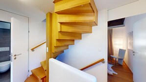 A modern staircase with wooden steps and a white handrail, leading to a room with a white door and a visible bathroom.