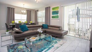 A modern living room with a sectional sofa, glass coffee table, and a dining area with a table and chairs.