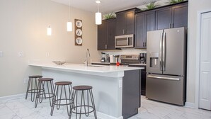 A modern kitchen with dark cabinets, a stainless steel refrigerator, a microwave, and a large island with bar stools.