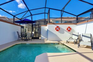 A swimming pool with a glass enclosure, lounge chairs, and a table with chairs. - Marvelous 5 Bedroom w Pool Close to Disney 4811 (Kissimmee)