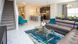 A modern living room with a brown leather sofa, a glass coffee table, and a teal rug.