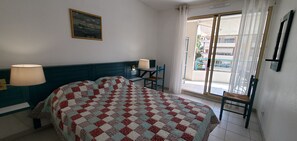 Une chambre d’hôtel avec un lit, deux lampes de chevet, une chaise, une table, un tableau au mur et une vue sur le balcon extérieur.
