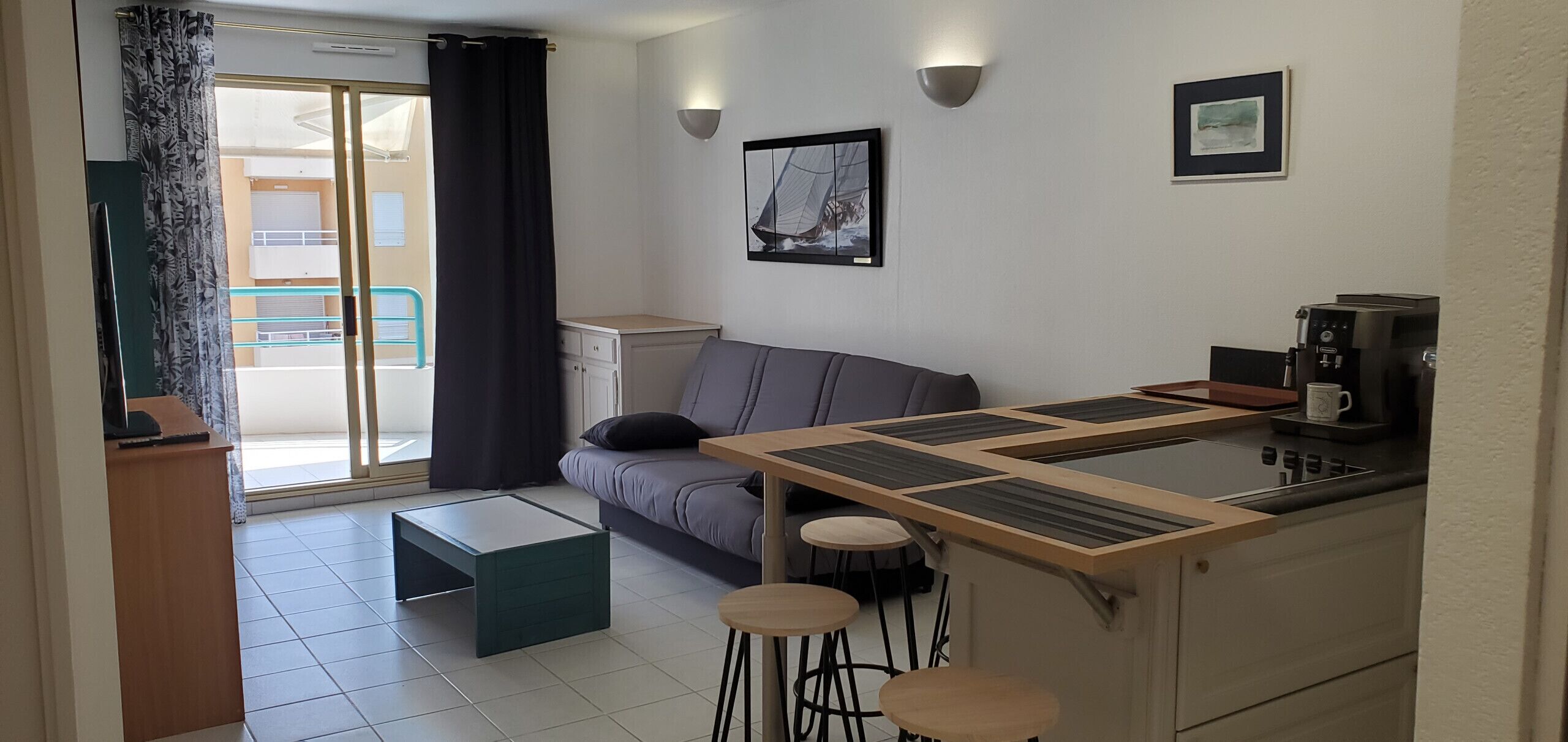 Un espace de vie compact comprenant un coin cuisine, un canapé, une machine à café et une vue sur l’extérieur.