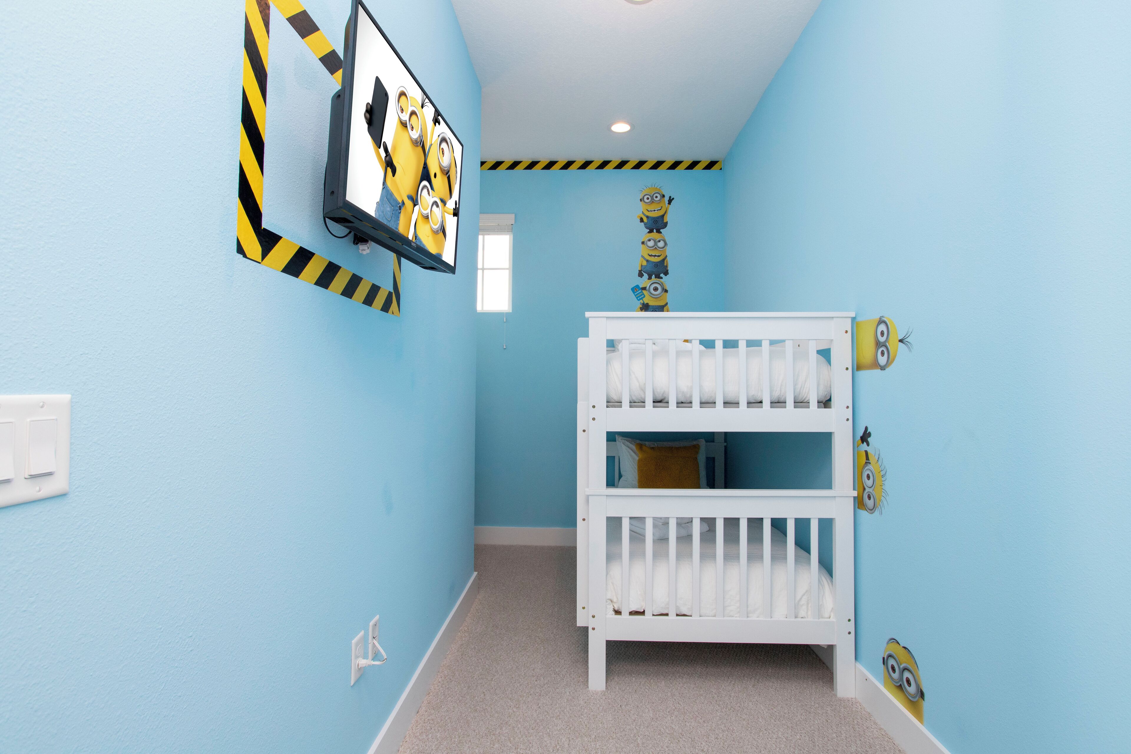 Una habitación con paredes azul claro, una cuna blanca y decoraciones con temática de los Minions.