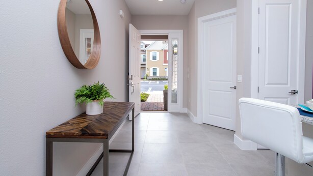 A hallway with a wooden console table, a potted plant, a round mirror, and a white chair. - Gorgeous 4 Bedroom Family Friendly Close to Disney 7573 (Kissimmee)