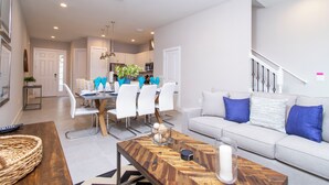 A modern living room with a sofa, coffee table, and dining area. - Gorgeous 4 Bedroom Family Friendly Close to Disney 7573 (Kissimmee)