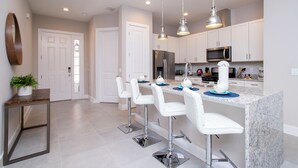 A modern kitchen with white bar stools, stainless steel appliances, and pendant lighting. - Gorgeous 4 Bedroom Family Friendly Close to Disney 7573 (Kissimmee)