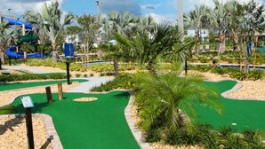 A golf course with a green putting area, palm trees, and a water slide in the background. - Stunning 5 Bd Home w Pool Close to Disney 4822 (Kissimmee)